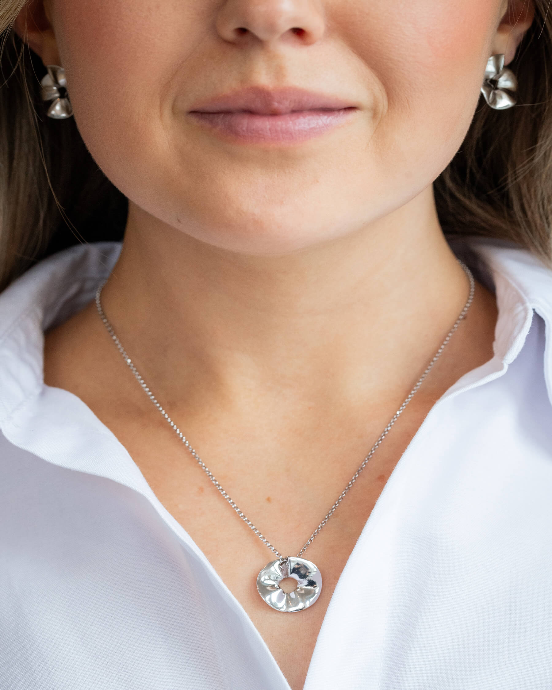 Leende kvinna i vit skjorta och större örhängen i silver samt halsband i silver.