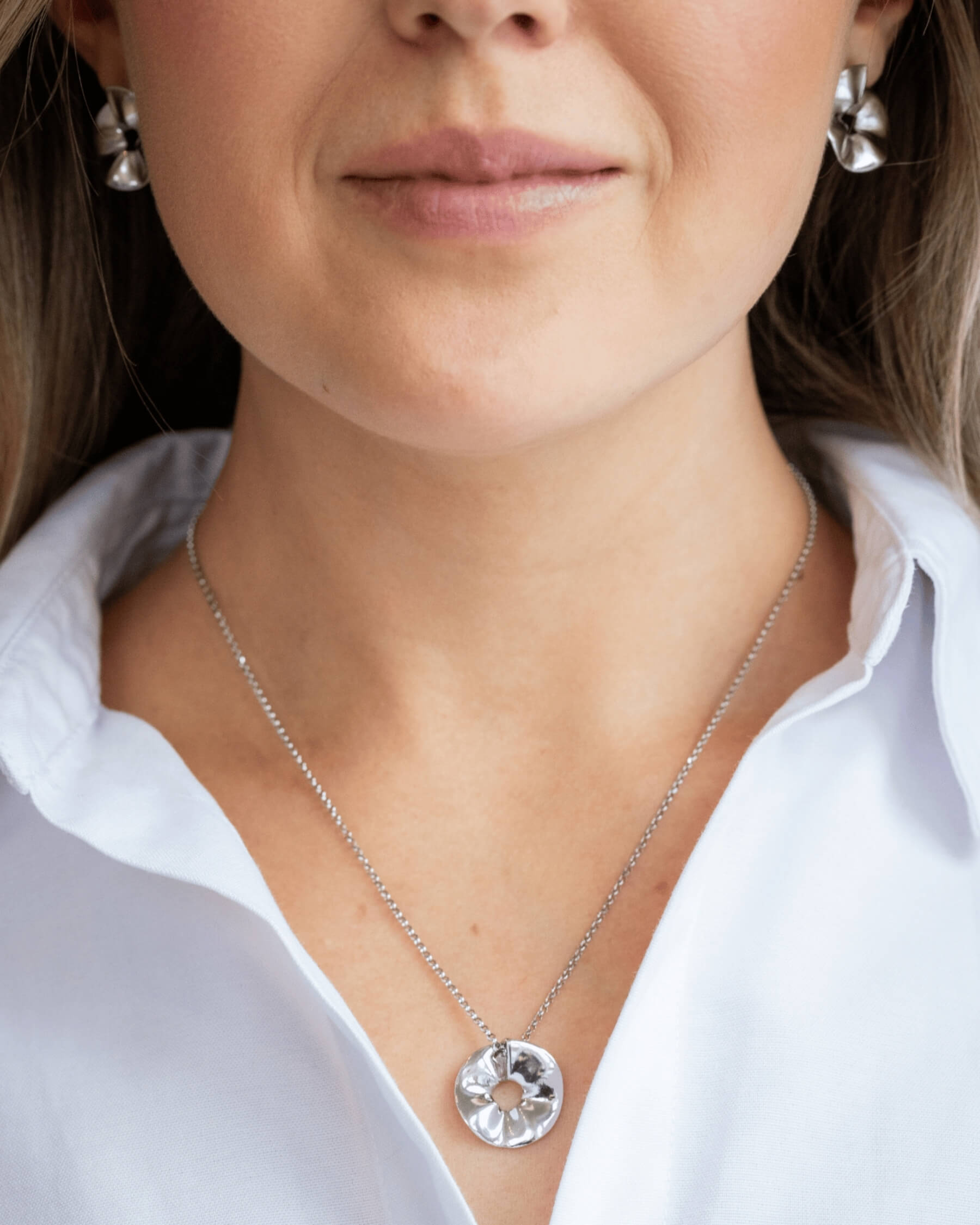 Leende kvinna i vit skjorta och större örhängen i silver samt halsband i silver.
