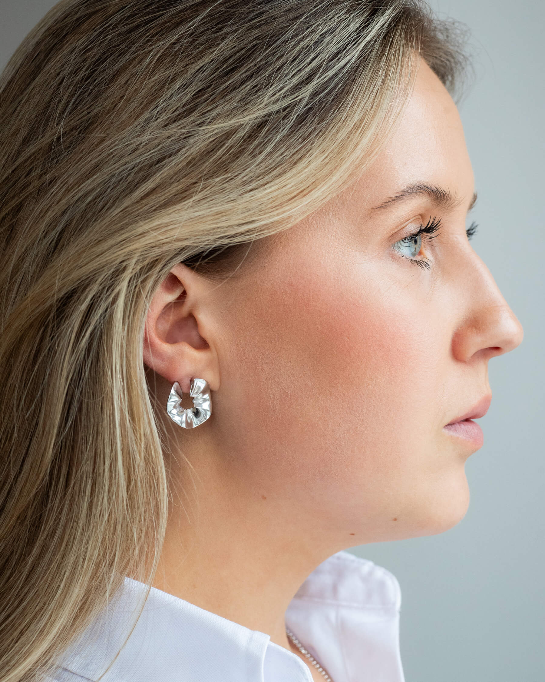 Kvinna i profil i vit skjorta och större örhängen i sterling silver.