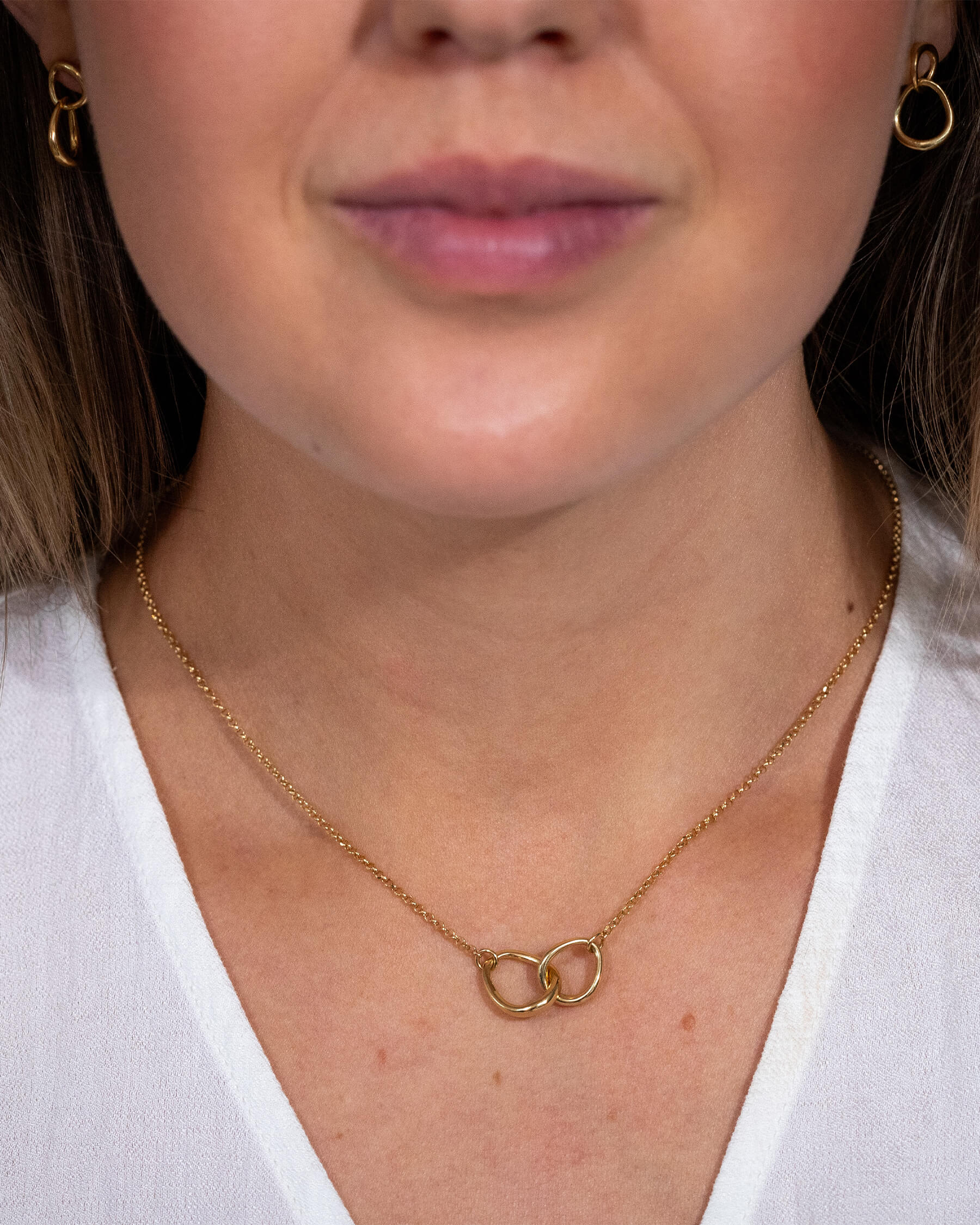 Kvinna med vit skjorta, hängande örhängen i guldpläterat sterling silver och halsband i guldpläterat silver.