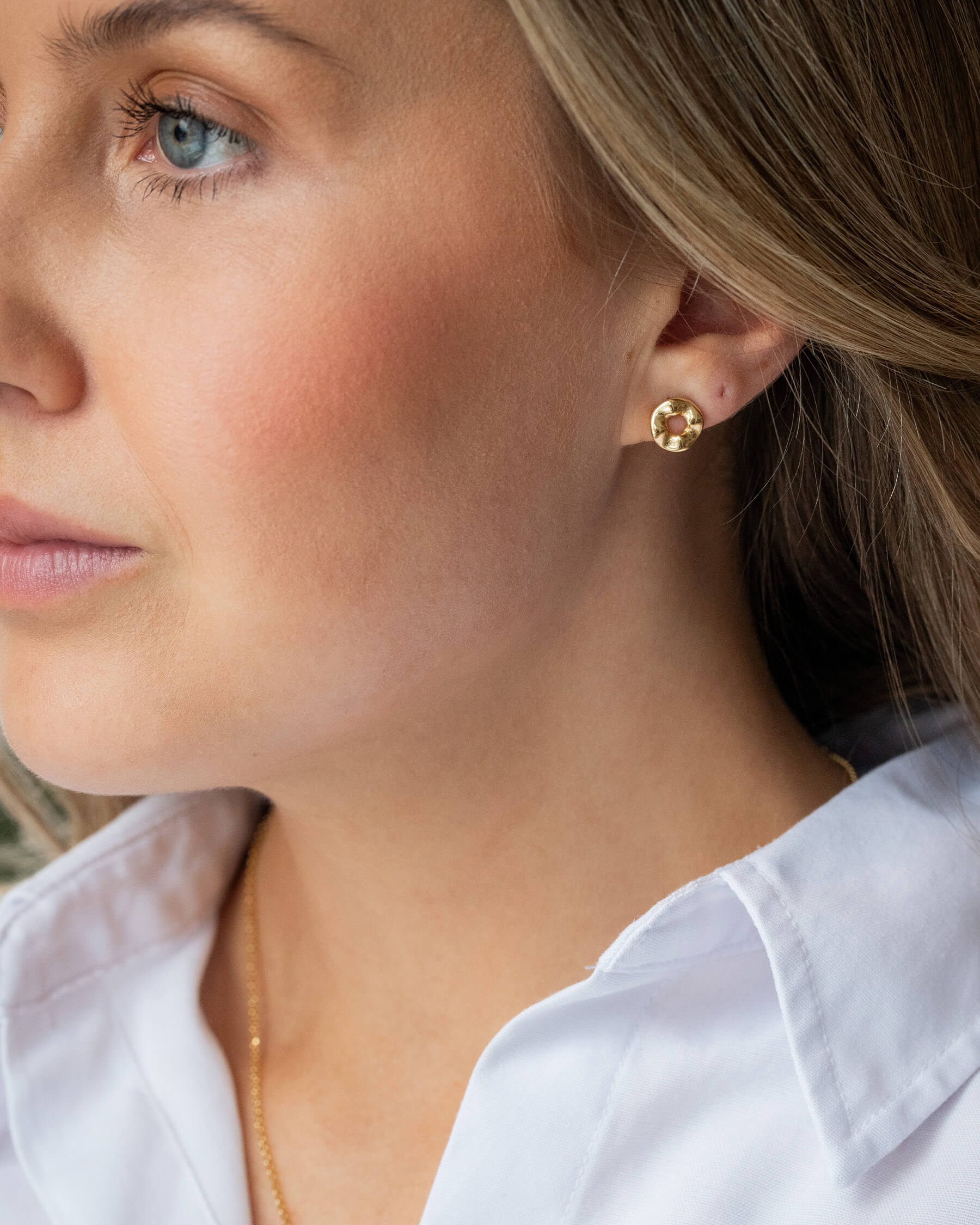 Kvinna i vit skjorta och örhängen i guldpläterat silver och halsband i guldpläterat silver.