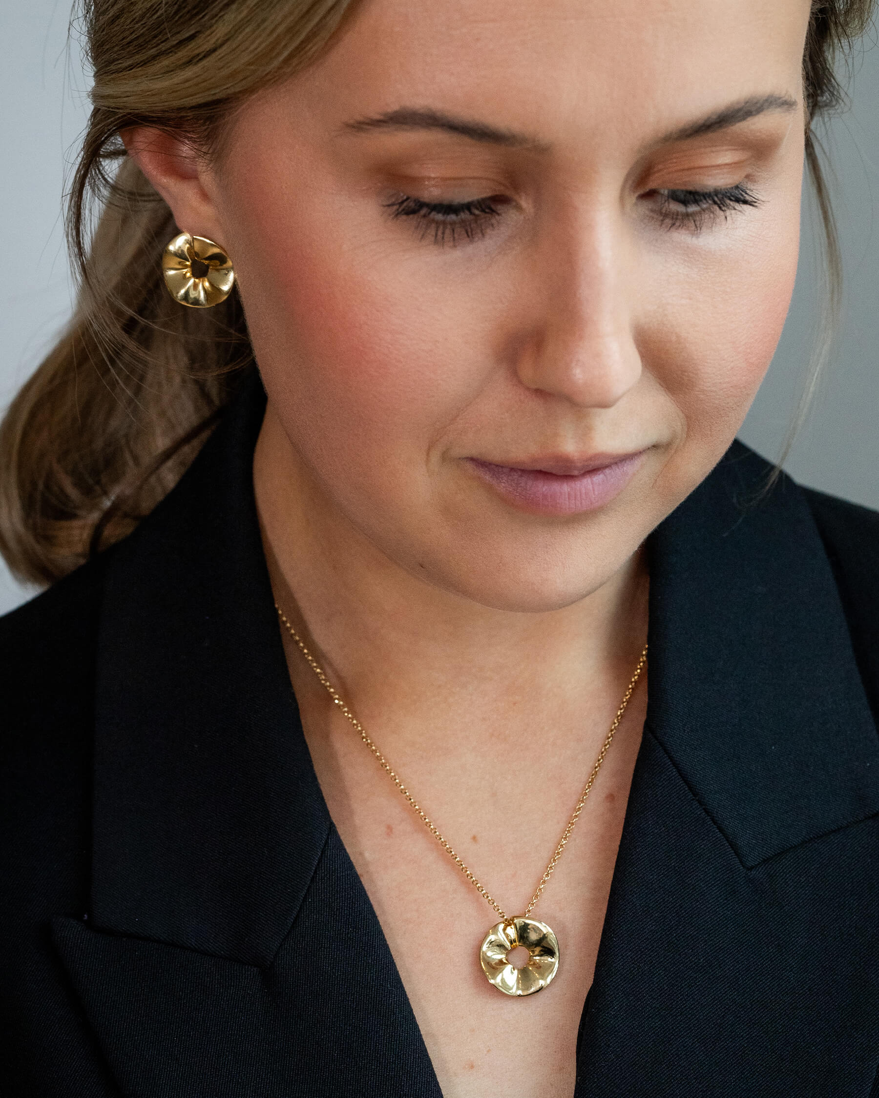 Kvinna i svart topp och större örhängen i guldpläterat silver och halsband i guldpläterat silver.