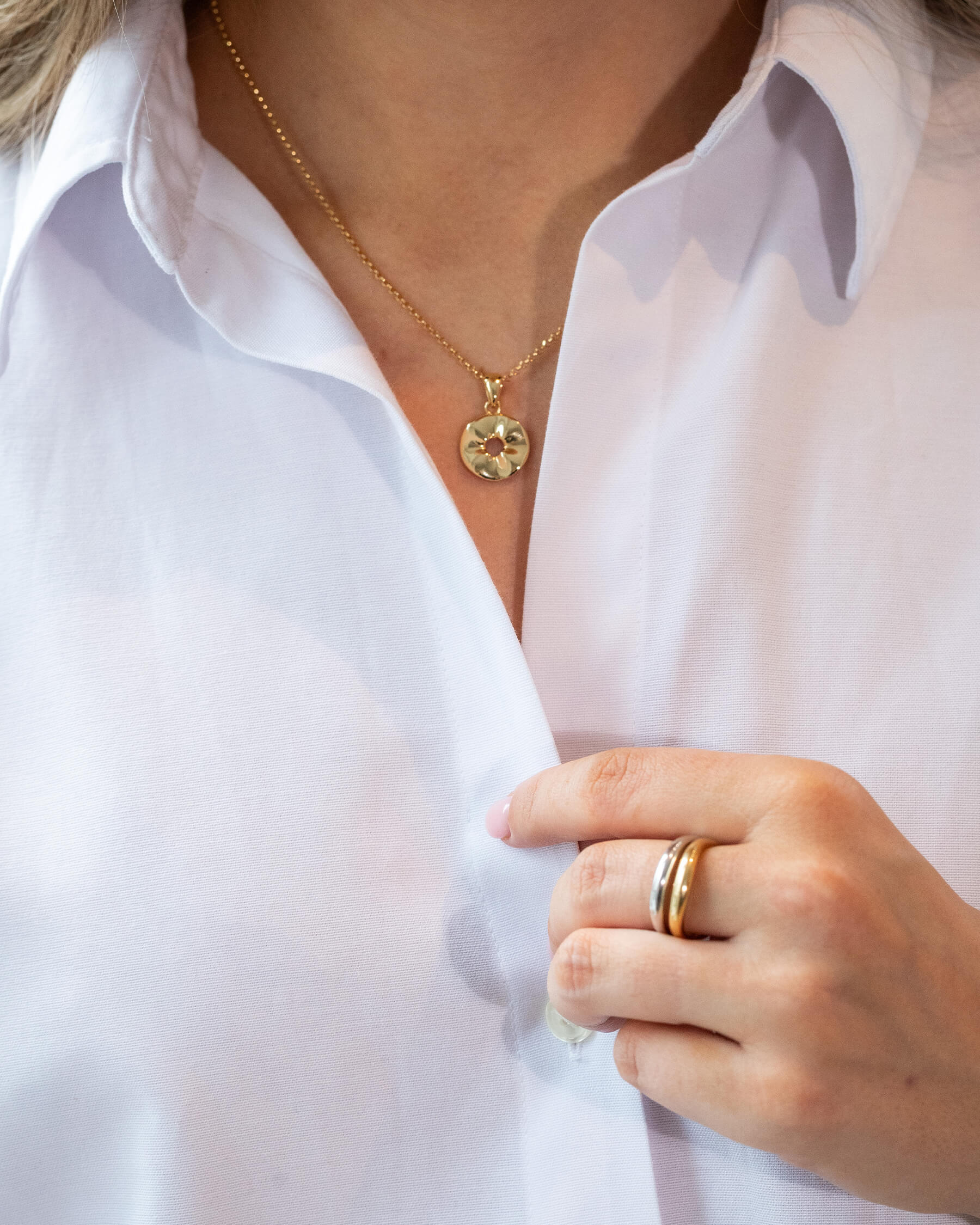 Kvinna i vit skjorta och halsband i gulddpläterat sterling silver och två ringar intill varandra i silver och guldpläterat silver.