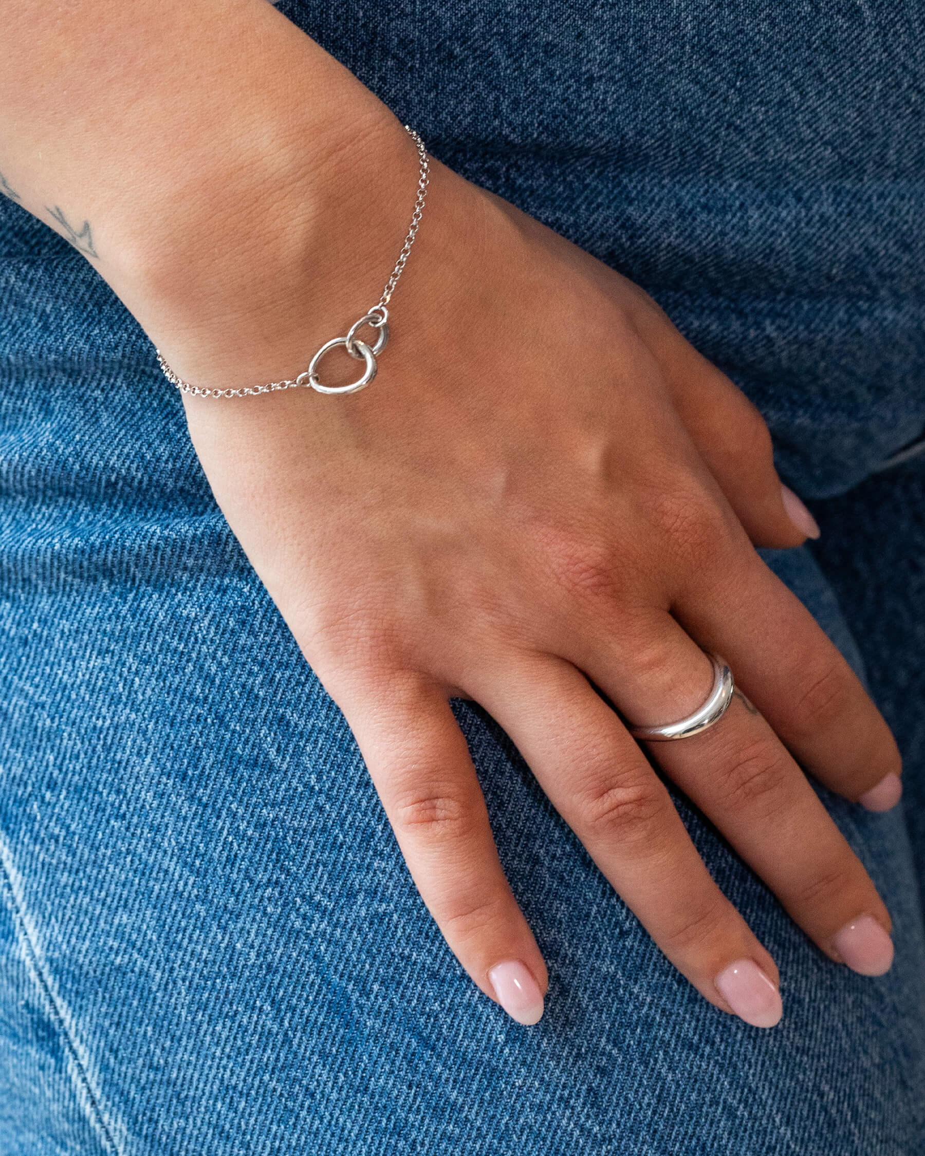 Kvinna med blå jeans, armband i silver och en ring i silver.
