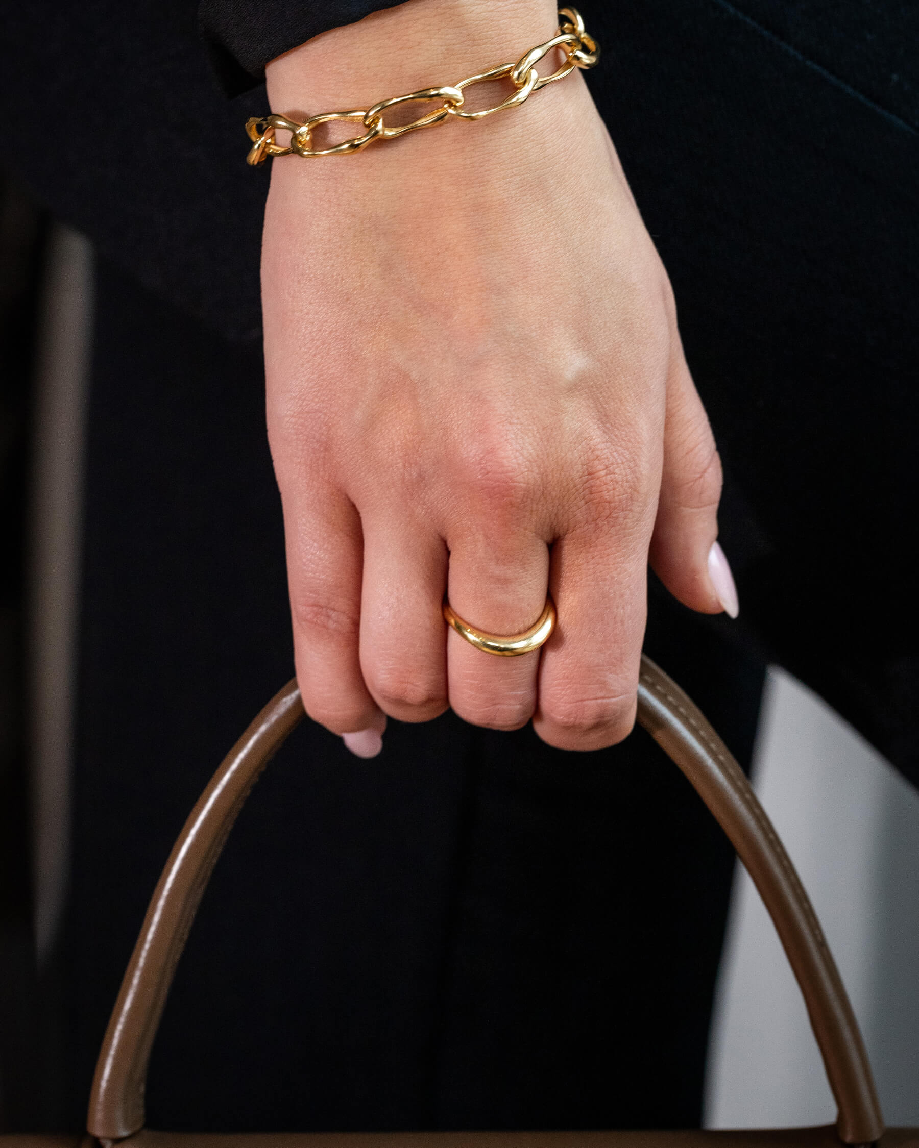Kvinna i svarta kläder, ring i guldpläterat silver och armband i guldpläterat silver som håller i en väska.