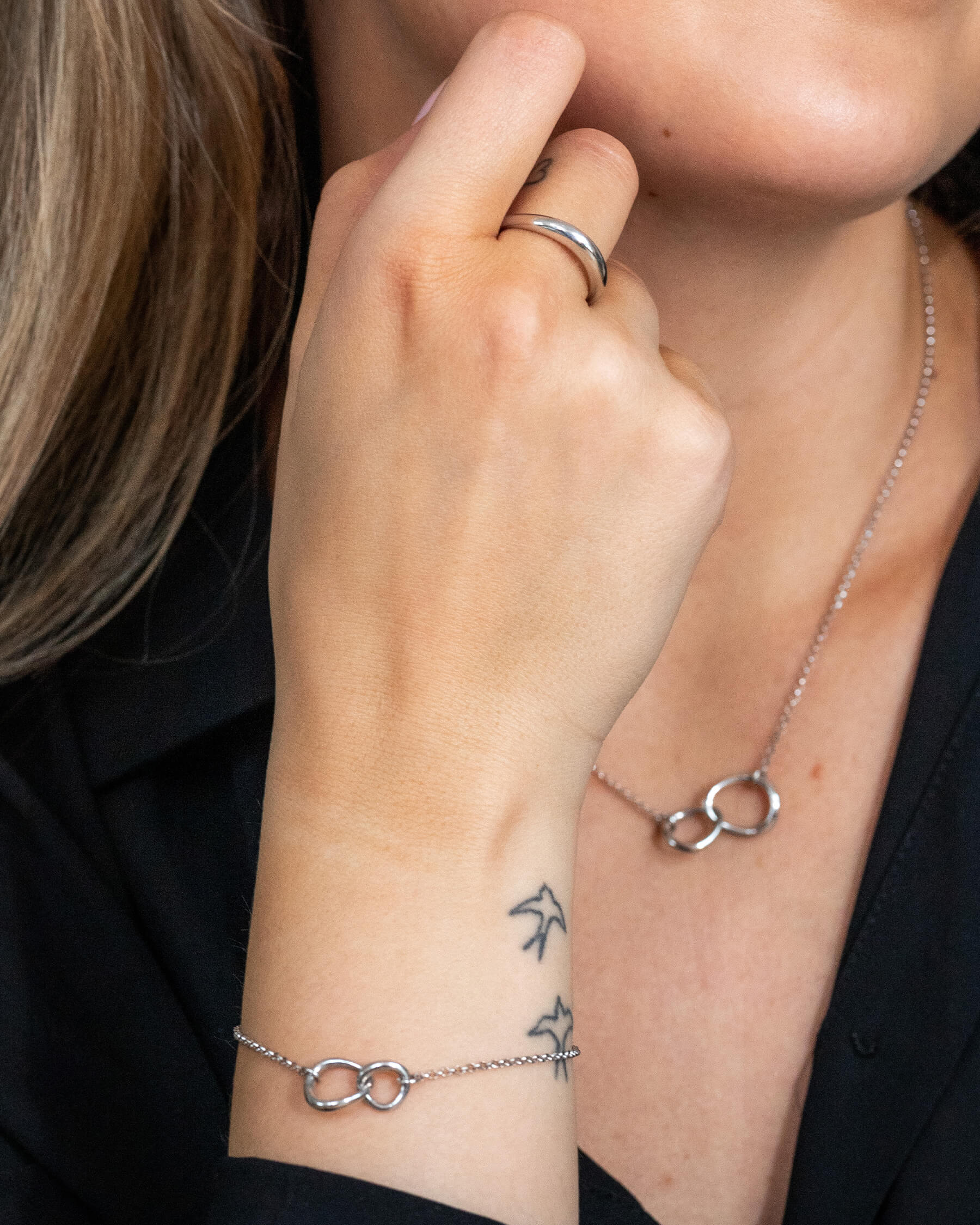 Kvinna i svart topp och halsband i silver, en ring i silver och ett armband i silver.