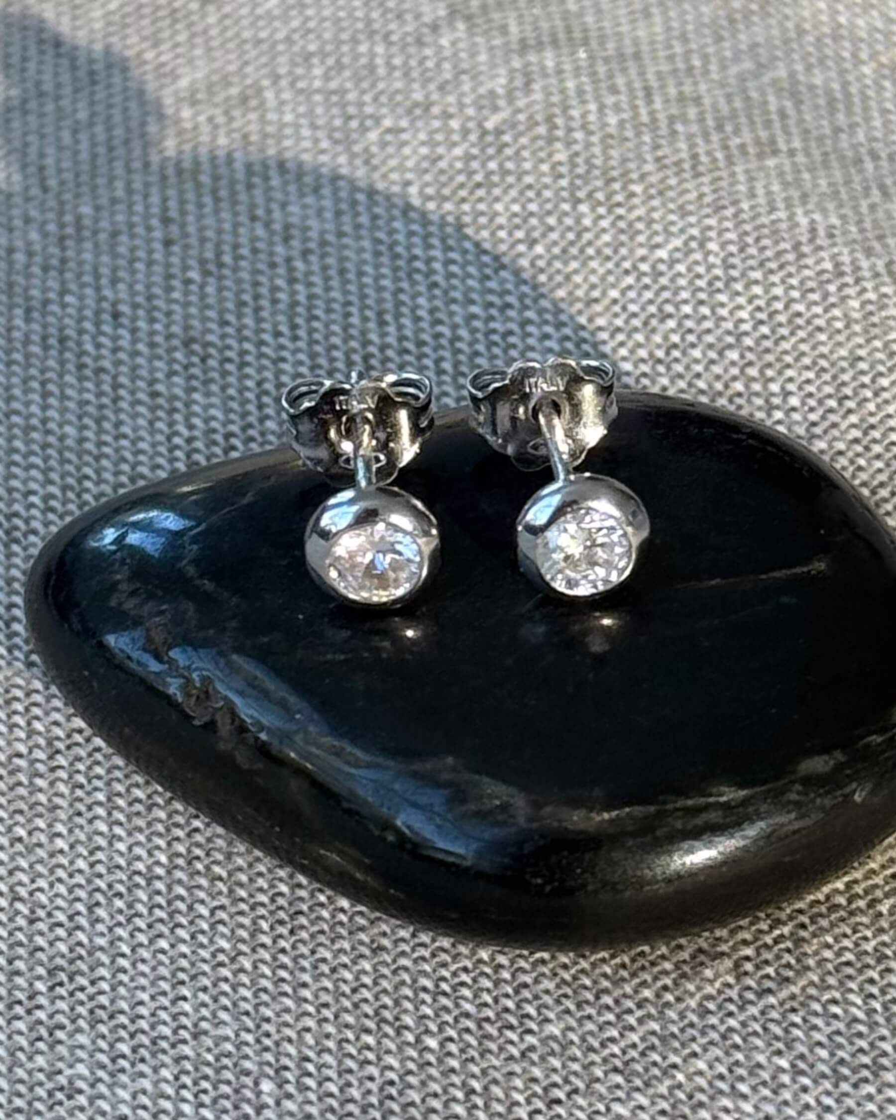 Örhängen med CZ (genomskinlig glaskristall) i rhodiumpläterat 925 sterling silver. Örhängena ligger på en svart sten.