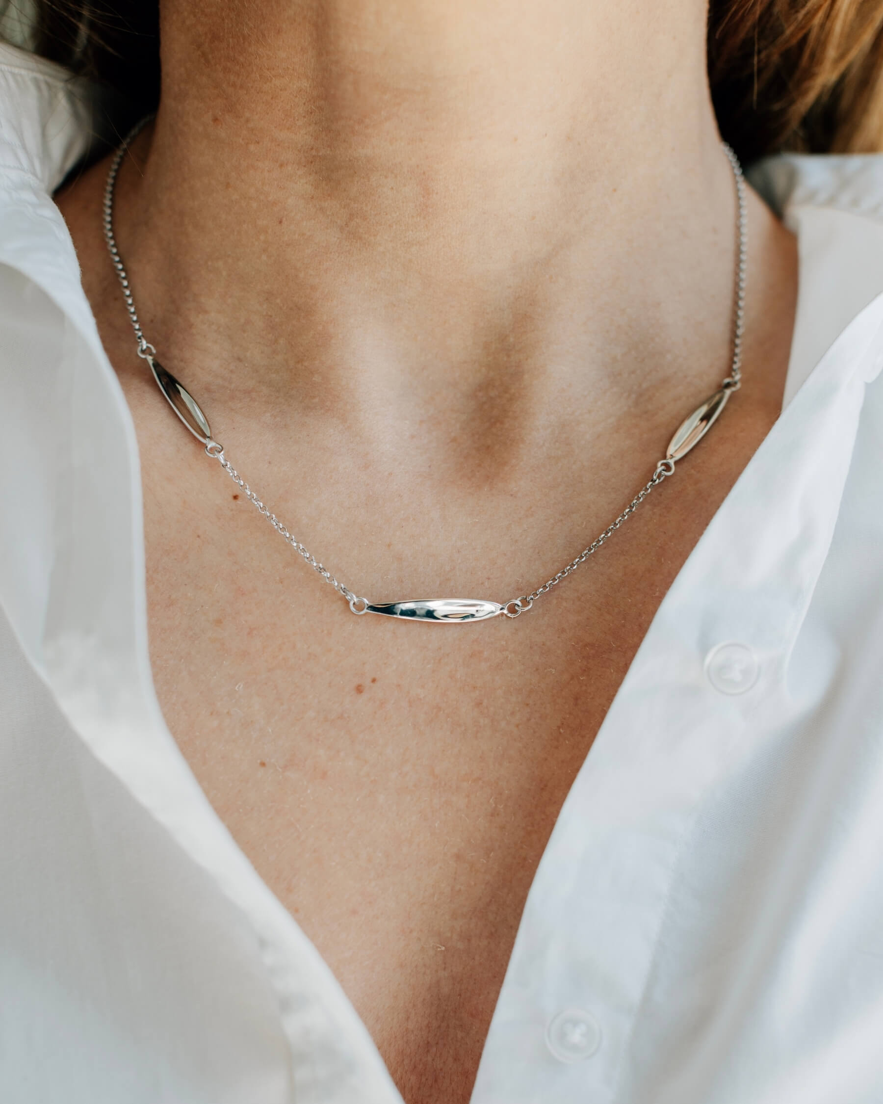 Närbild på en hals som bär ett elegant halsband med tunn kedja och tre olivbladsformade plattor, tillverkat rhodiumpläterat 925 sterling silver.
