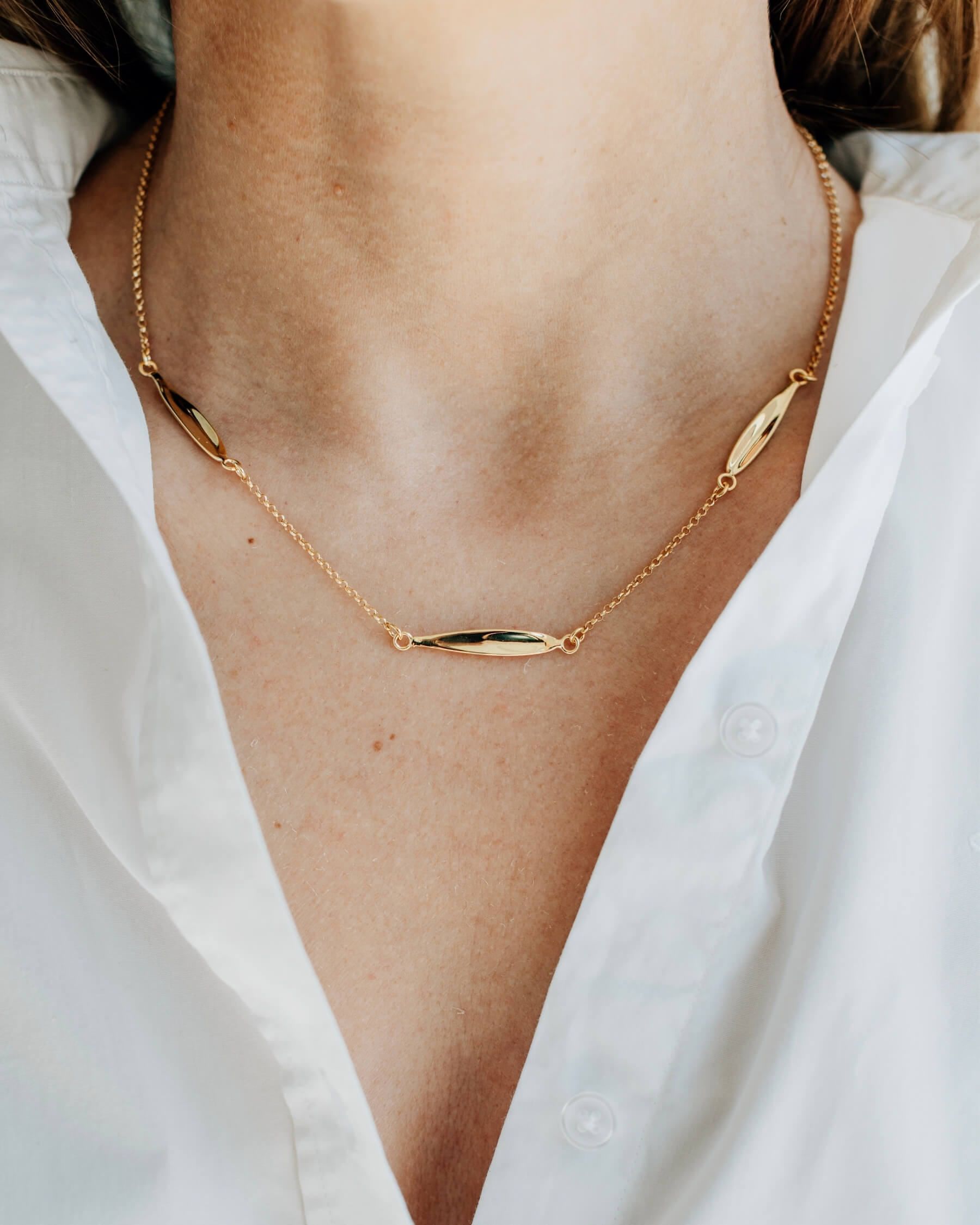 Närbild på en hals som bär ett elegant halsband med tunn kedja och tre olivbladsformade plattor, tillverkat guldpläterat 925 sterling silver.