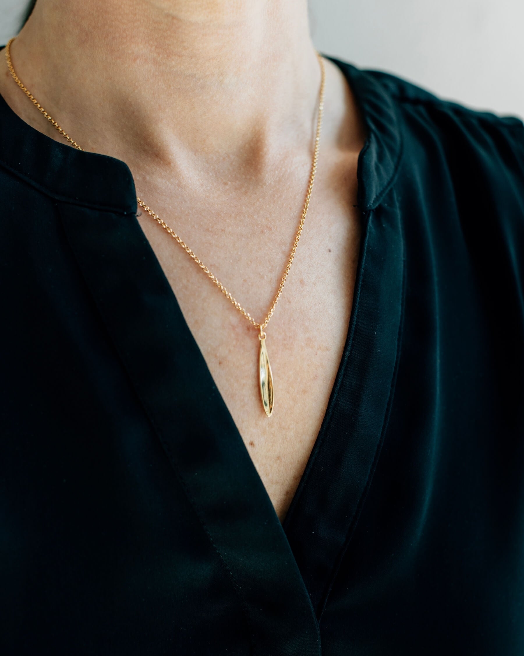 Närbild på en hals som bär ett elegant halsband med tunn kedja och ett hängsmycke i form av ett olivblad, tillverkat guldpläterat 925 sterling silver.