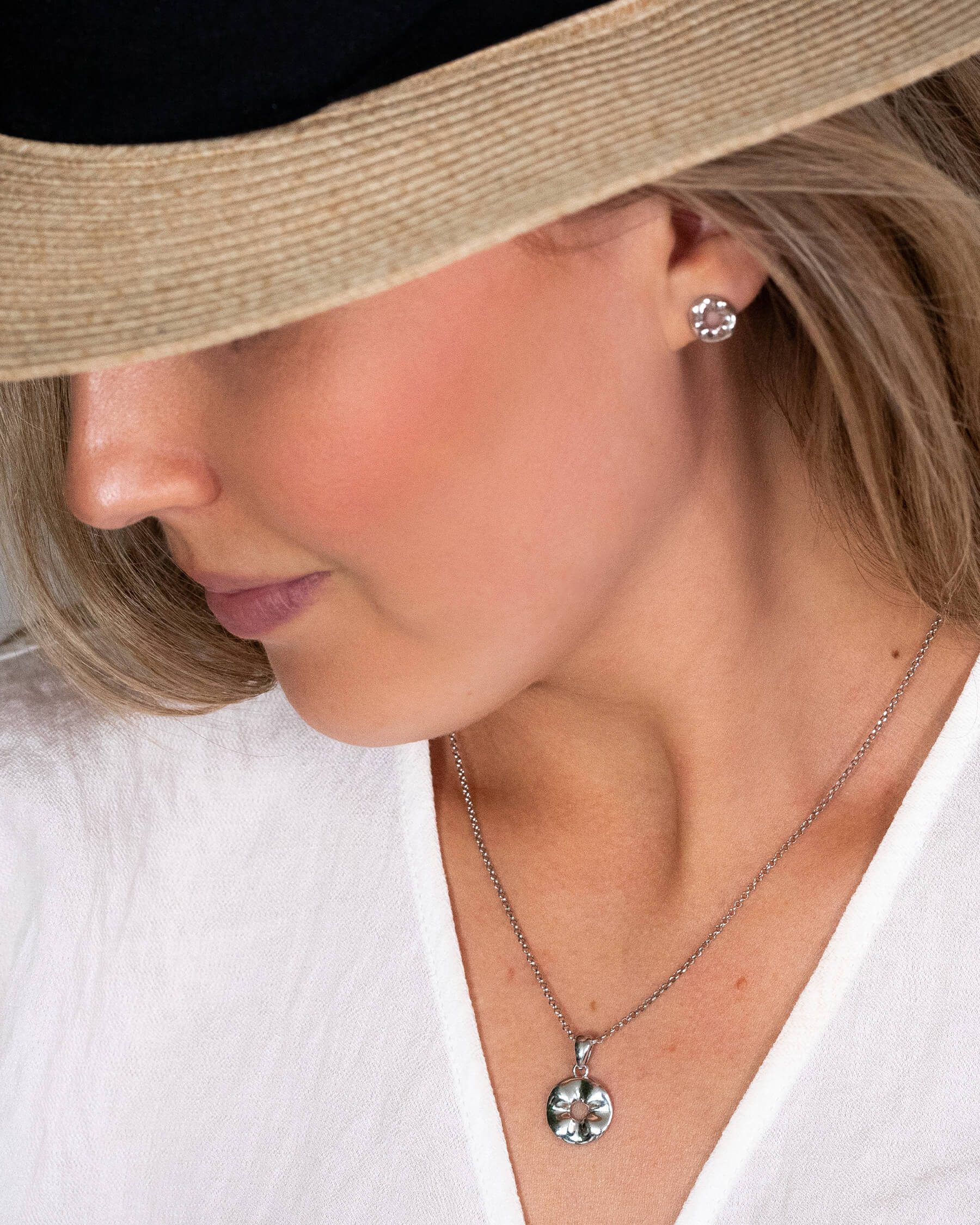 Kvinna i vit topp och stråhatt med halsband i silver och örhängen i silver.