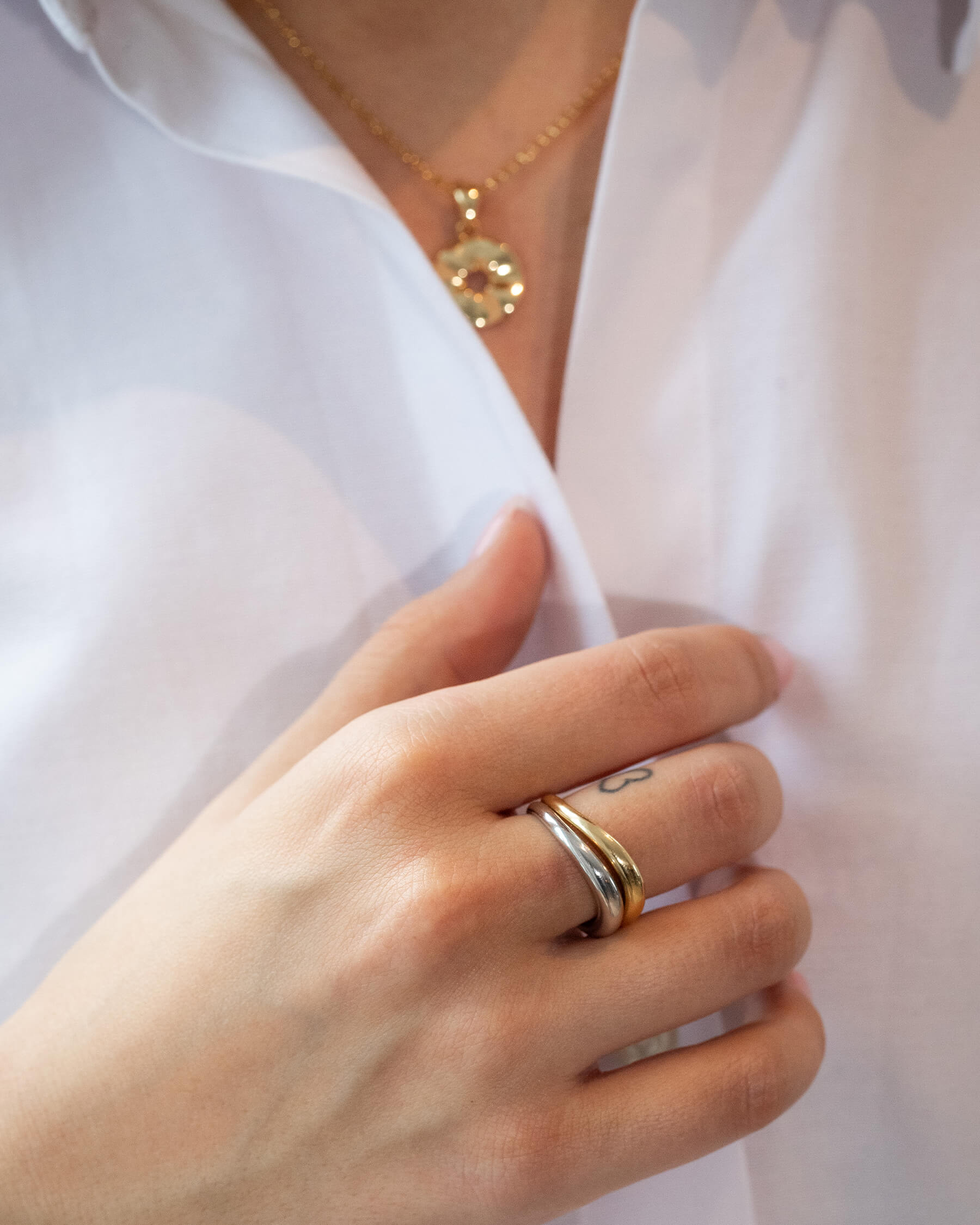 Kvinna i vit skjhorta och halsband i guldpläterat silver och två matchande ringar på fingret i silver och guldpläterat silver.