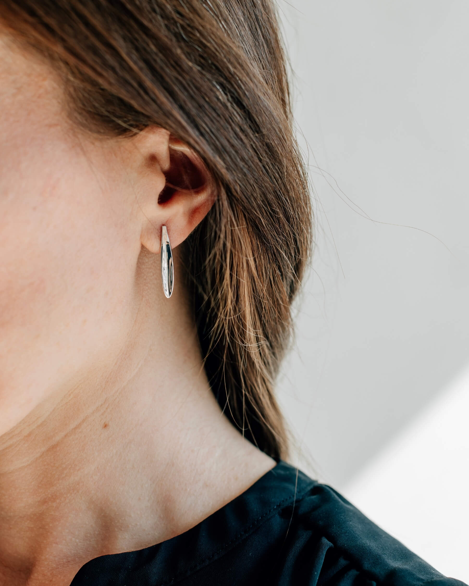 Närbild på ett öra som bär ett örhängen med olivbladsformad platta i rhodiumpläterat 925 Sterling silver.