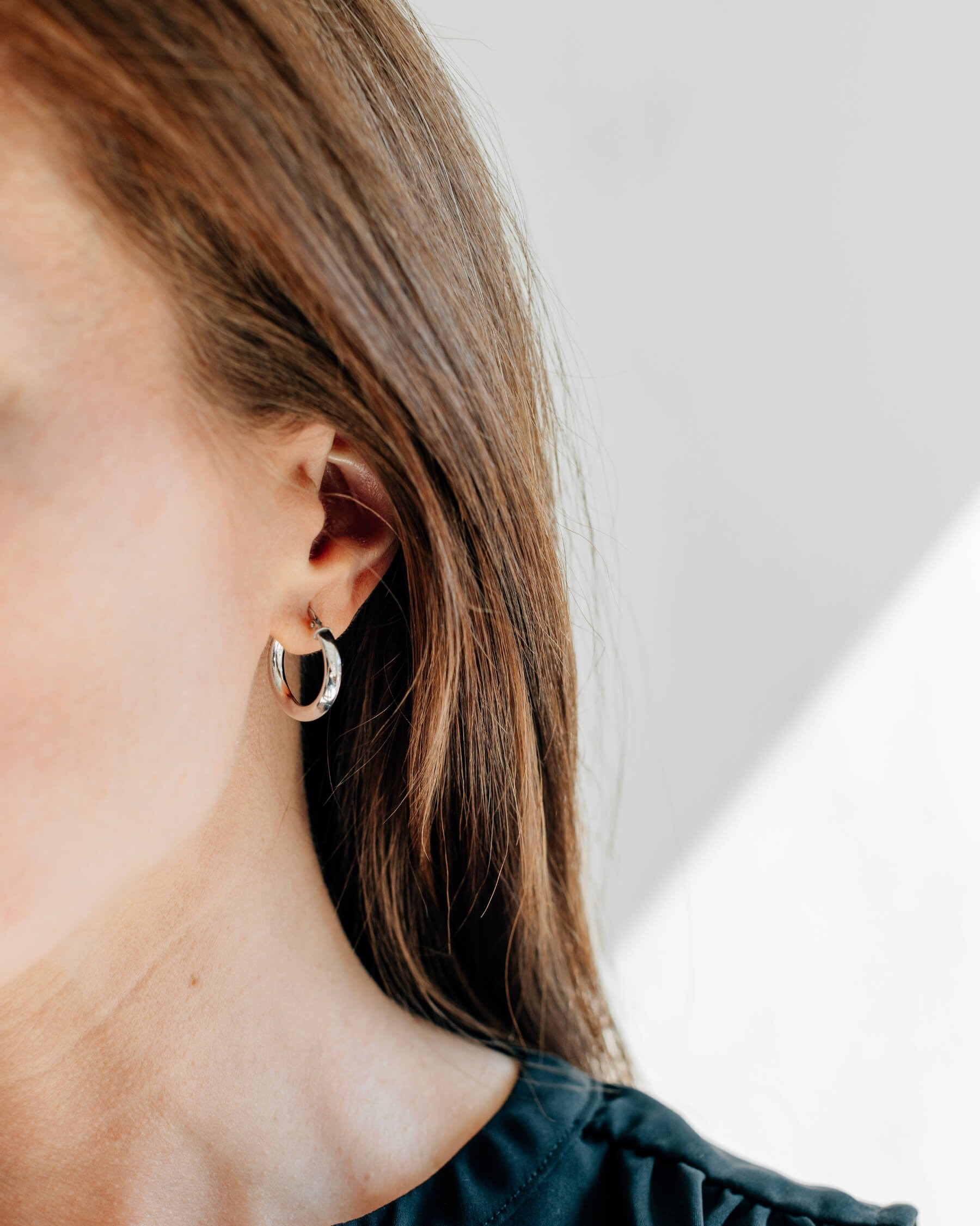 Närbild på ett öra som bär ett runt, lätt vridet, örhängen (hoop) i rhodiumpläterat 925 Sterling silver.