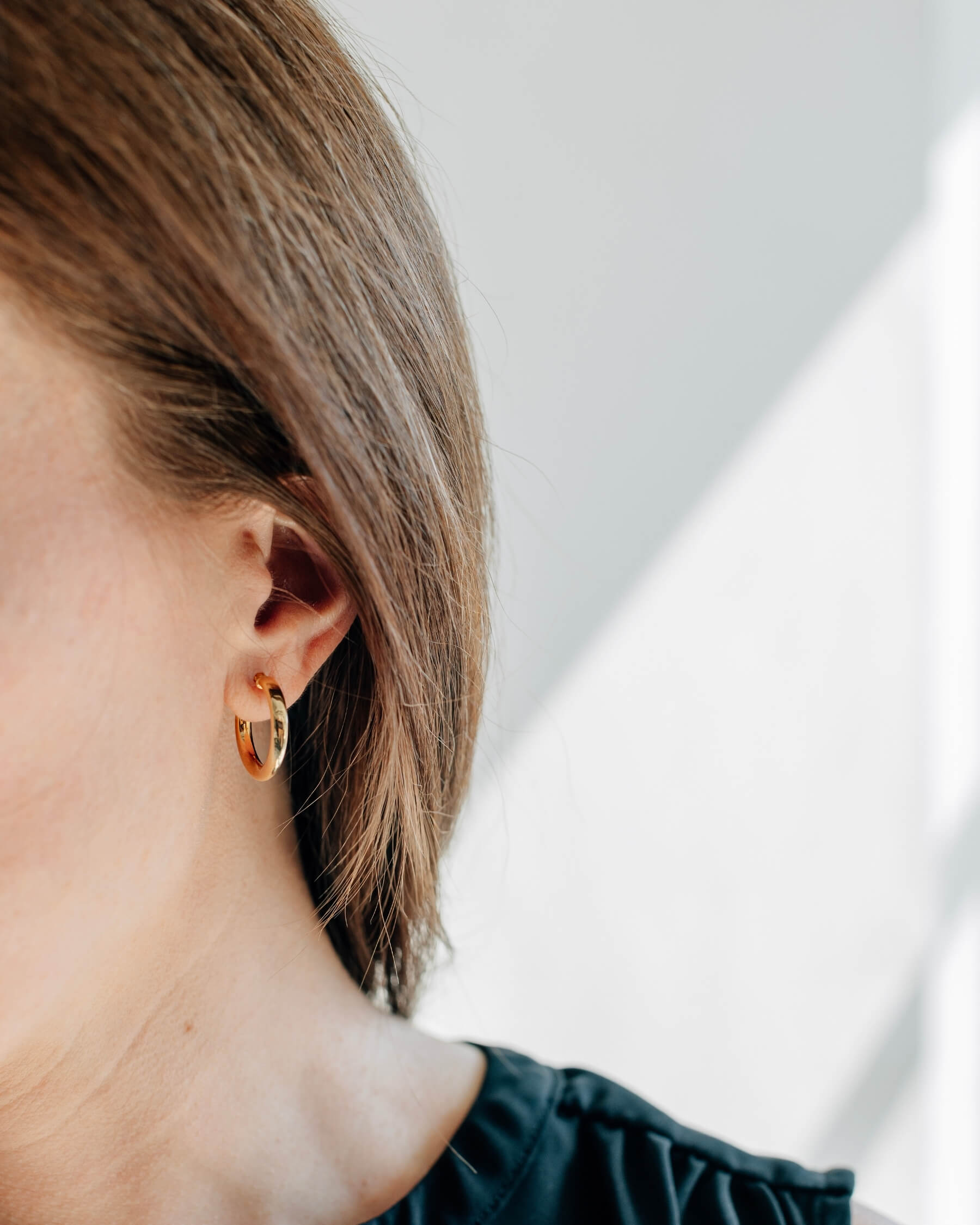 Närbild på ett öra som bär ett runt, lätt vridet, örhängen (hoop) i guldpläterat 925 Sterling silver.