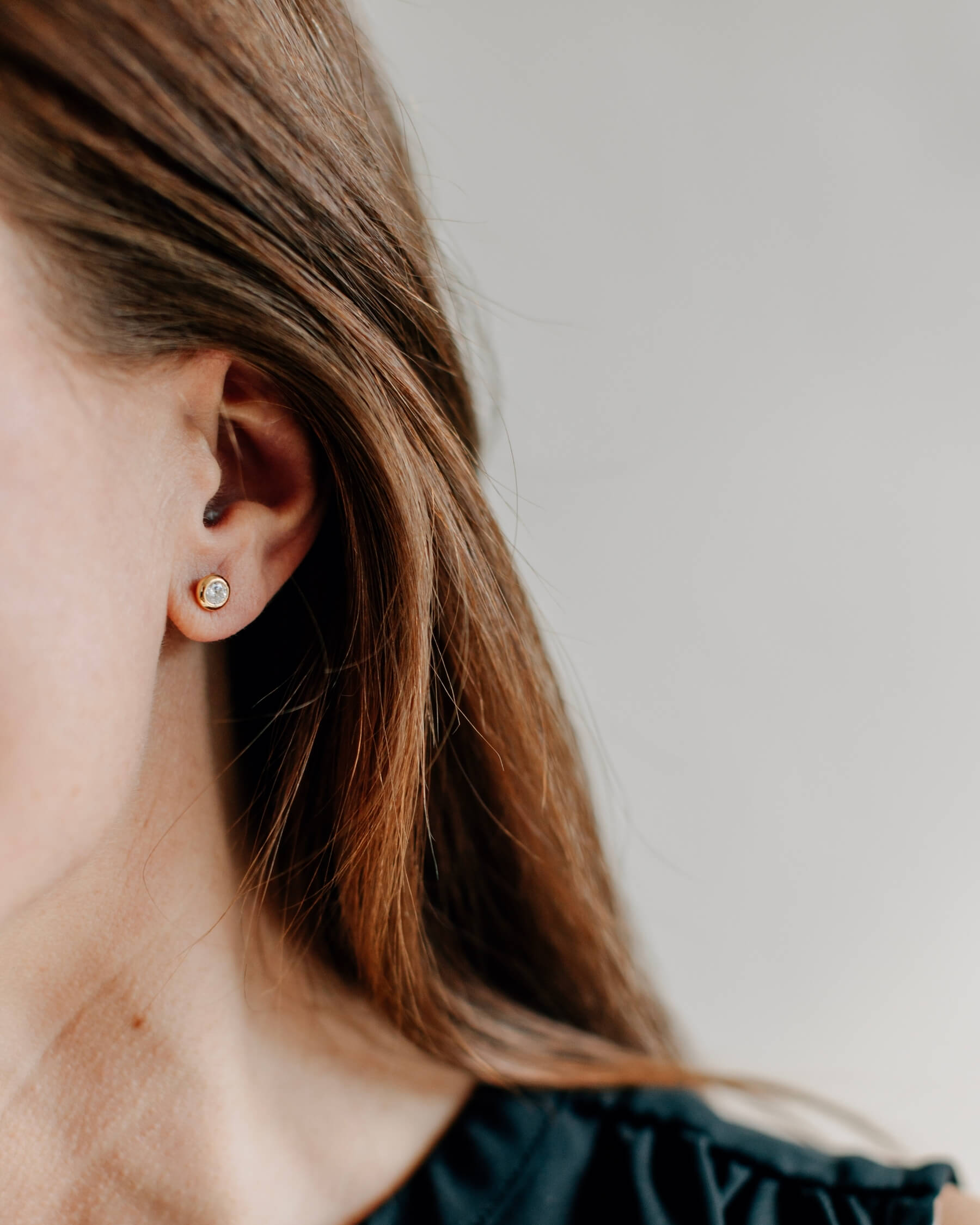 Närbild på ett öra som bär ett örhänge med en rund, vit kubisk zirkonia i guldpläterat 925 Sterling silver.