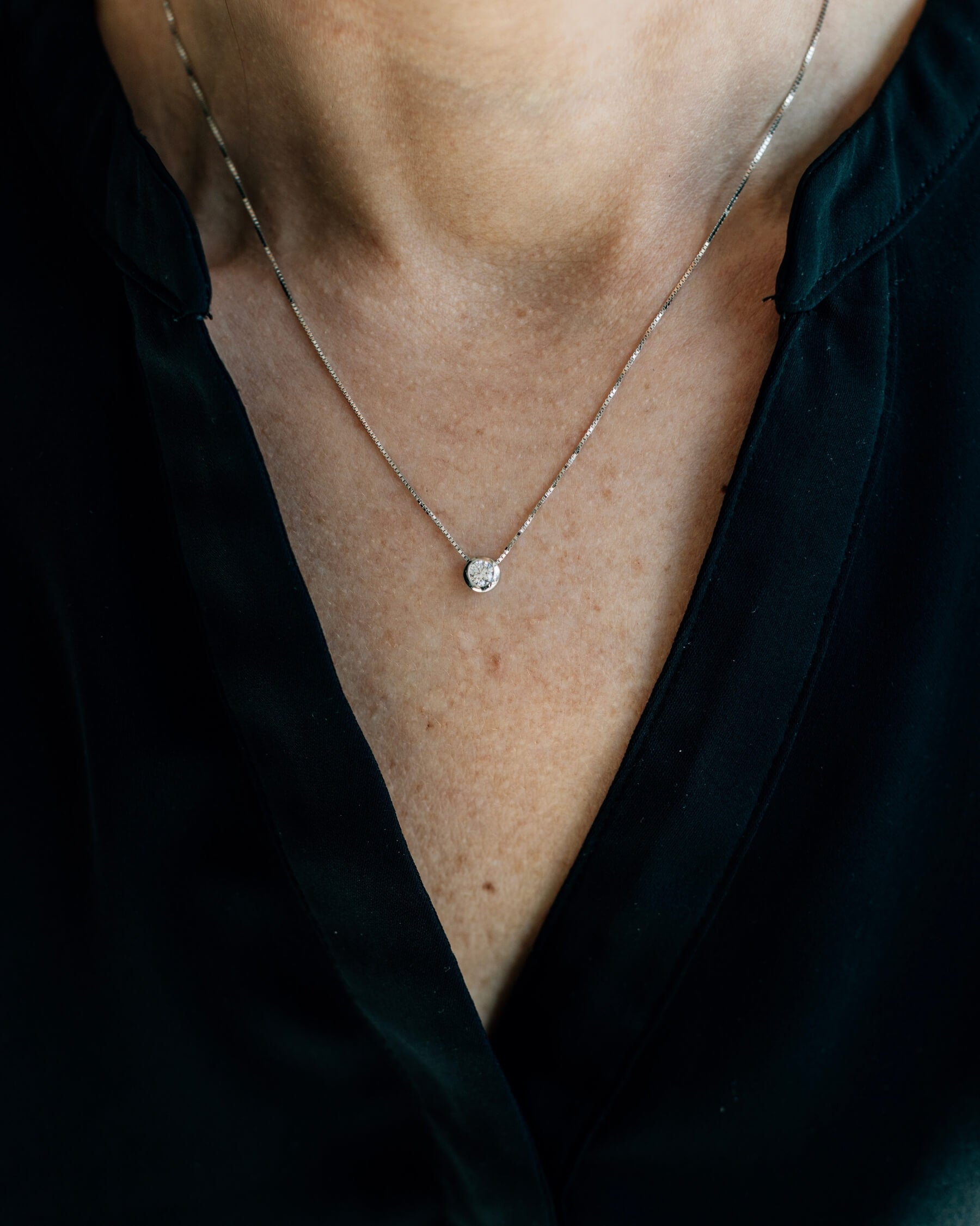 Närbild på en hals som bär ett halsband med tunn kedja och en rund, vit kubisk zirkonia i rhodiumpläterat 925 Sterling silver.