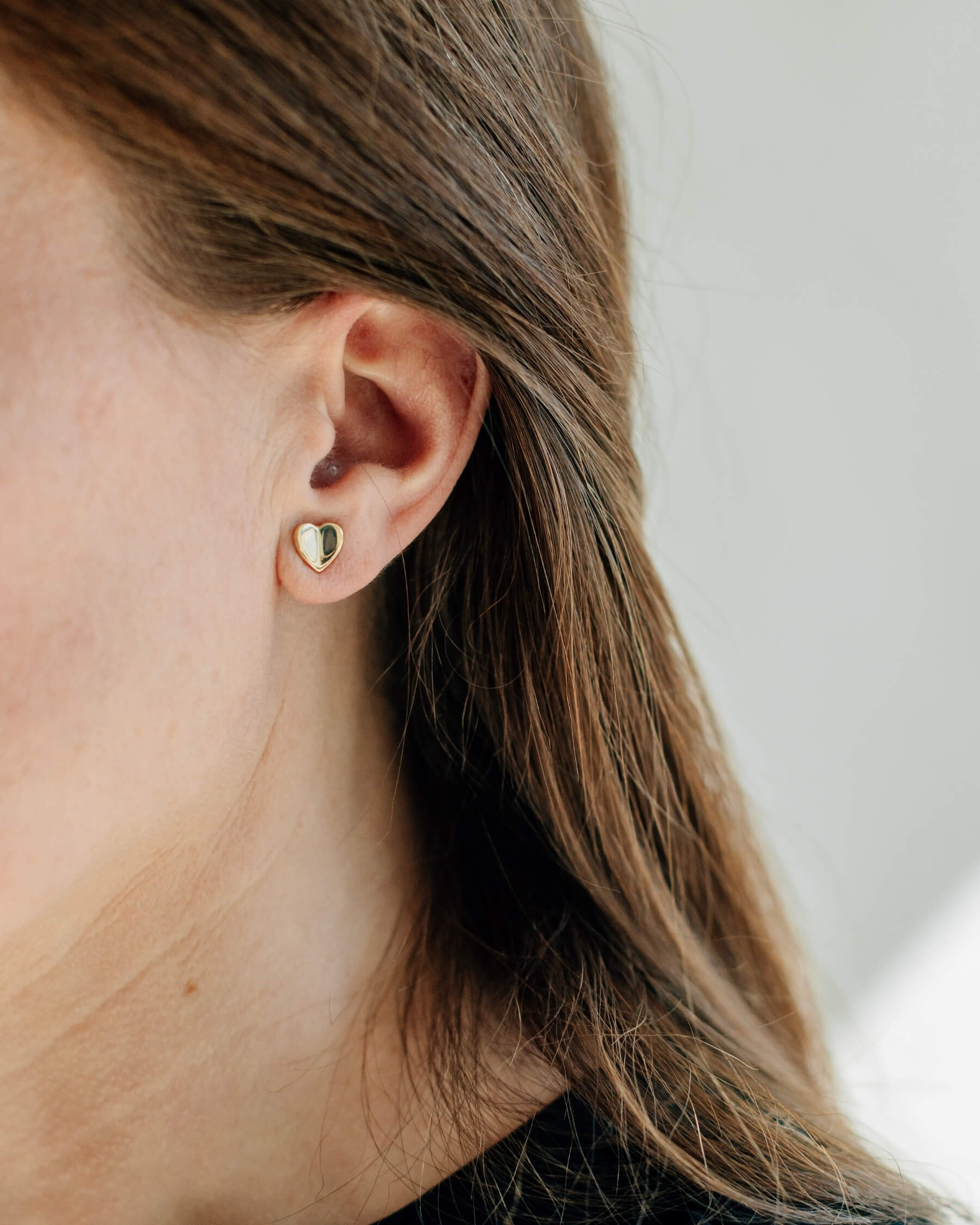 Närbild på ett öra som bär ett örhänge i form av ett hjärta, tillverkat i guldpläterat 925 sterling silver.