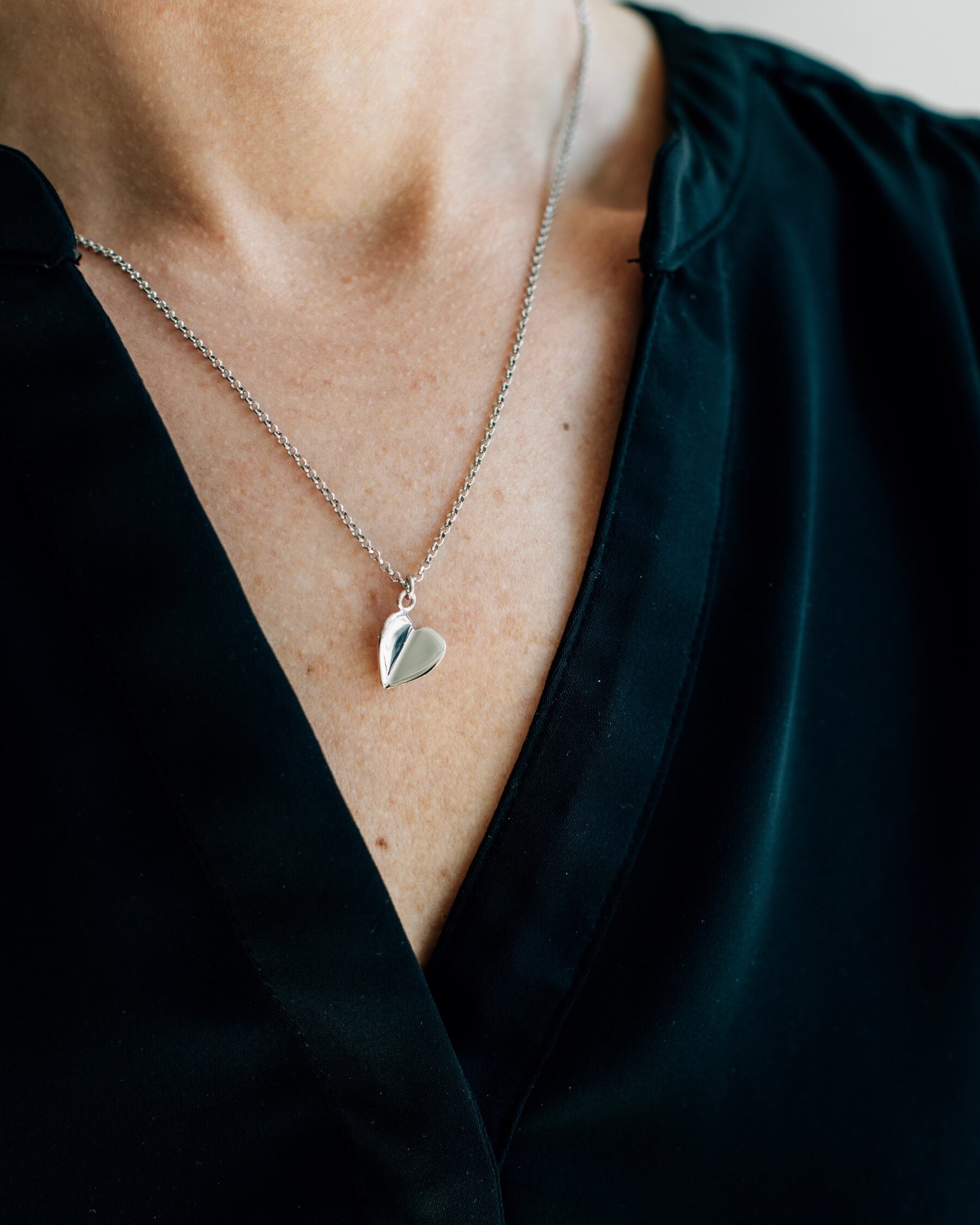 Närbild på en hals som bär ett elegant halsband med tunn kedja och ett hängsmycke i form av ett hjärta, tillverkat rhodiumpläterat 925 sterling silver.
