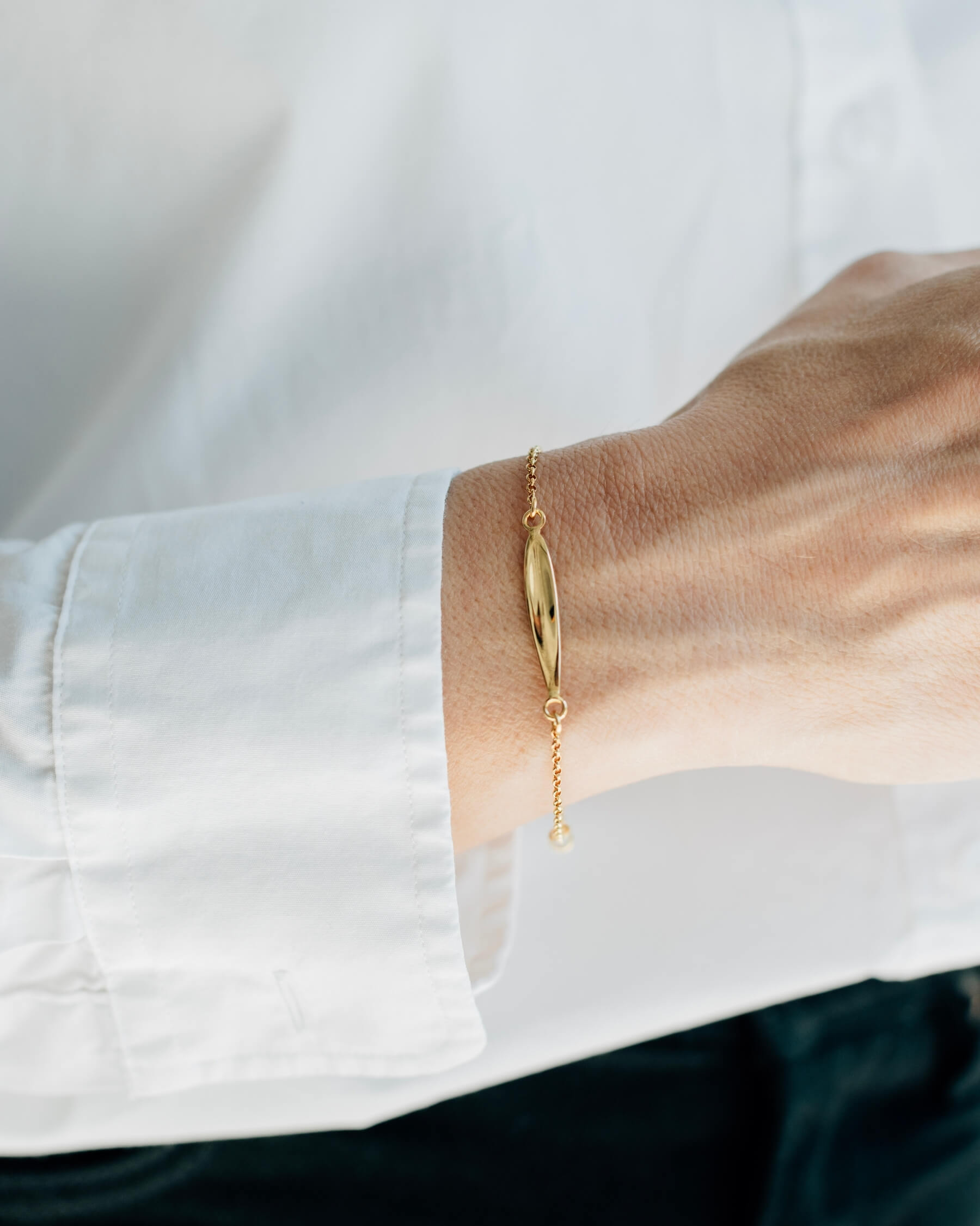 Närbild på en handled som bär ett elegant armband med tunn kedja och en blank olivbladsformad platta, tillverkat i guldpläterat 925 sterling silver.